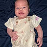 Xylin is registered to the contest to win money with this photo: baby, child, infant, smiling, happy, portrait, lying_down, blanket, blue_blanket, romper, striped_clothing, floral_pattern, clothing, face, eyes, hands, indoor, close_up, cheerful, photography