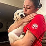 June is registered to the contest to win money with this photo: person, puppy, dog, pet, indoor, hug, affection, red_shirt, cute, animal, love, face, fur, cozy, home, comfort, young_animal, human, casual, holding