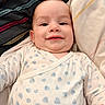 James participe au concours pour gagner de l'argent avec cette photo : baby, infant, smile, face, onesie, heart_pattern, bed, pillow, striped, fabric, cute, chubby_cheeks, lying_down, happy, child, skin, person, clothing, indoors, portrait