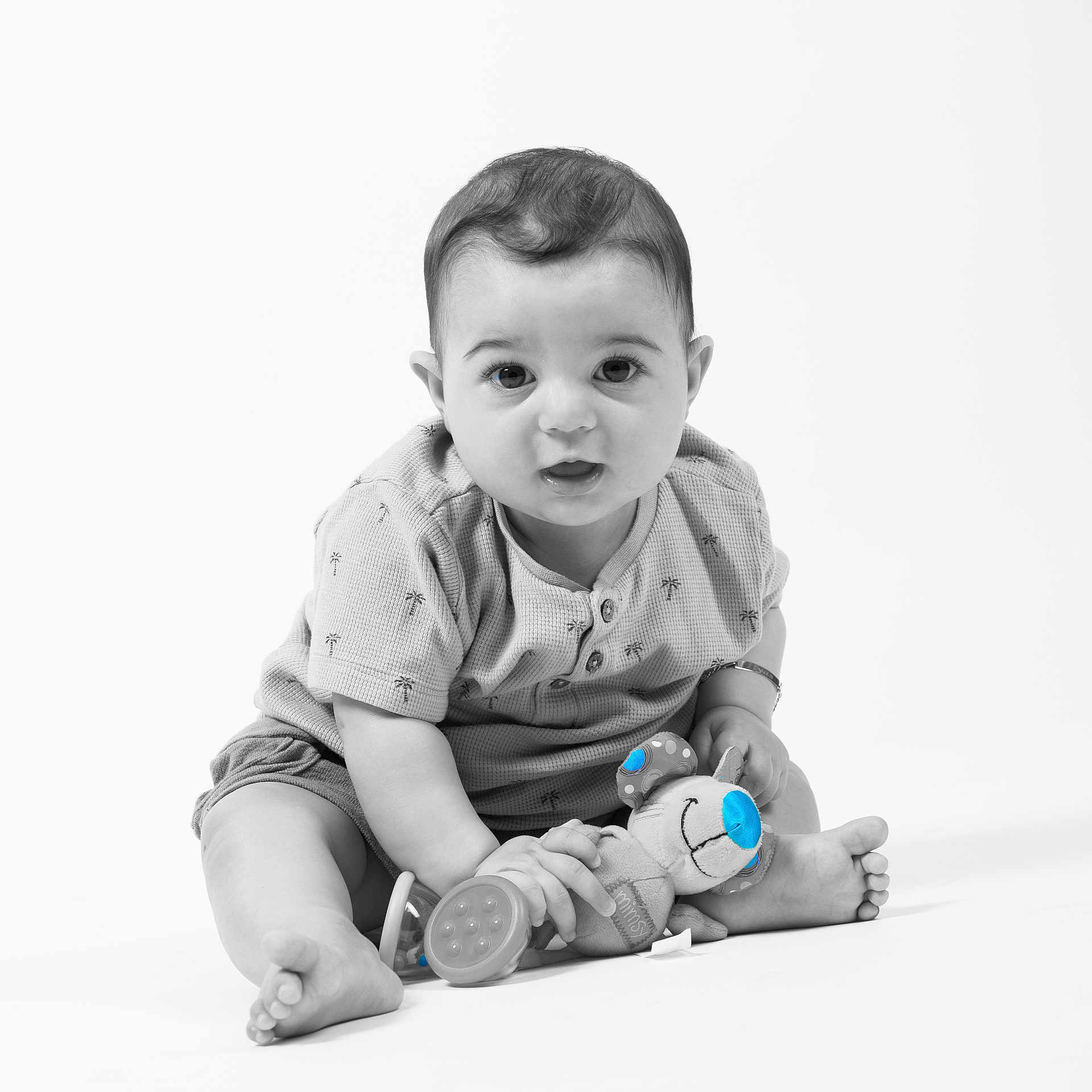 Ilyas participe au concours pour gagner de l'argent avec cette photo : baby, barefoot, black_and_white, blue_accent, bracelet, child, curly_hair, cute, infant, isolated, looking_at_camera, minimalist, plush_toy, portrait, shirt, shorts, sitting, smiling, studio, toy