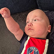 Nolhan participe au concours pour gagner de l'argent avec cette photo : baby, infant, child, face, arm, hand, couch, sofa, fabric, clothing, onesie, logo, paris_saint_germain, sportswear, portrait, indoors, cheek, gaze, lying_down, reaching