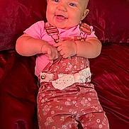 Samantha is registered to the contest to win money with this photo: baby, smiling, infant, pink_clothing, overalls, floral_pattern, happy, cute, child, portrait, lying_down, red_blanket, indoors, skin, face, hands, blue_eyes, short_hair, button, lace_bow