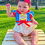 child, baby, toddler, smiling, red_bow, headband, dress, snow_white_costume, sitting, wooden_crate, grass, outdoor, park, sunlight, fence, portrait, feet, legs, hand_raised, cute