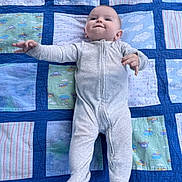 Braxton is registered to the contest to win money with this photo: baby, infant, onesie, quilt, patchwork, blue, smile, lying_down, child, cute, happy, fabric, pattern, blanket, person, young, reaching, indoor, cozy, soft