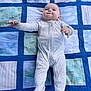 baby, infant, onesie, quilt, patchwork, blue, smile, lying_down, child, cute, happy, fabric, pattern, blanket, person, young, reaching, indoor, cozy, soft