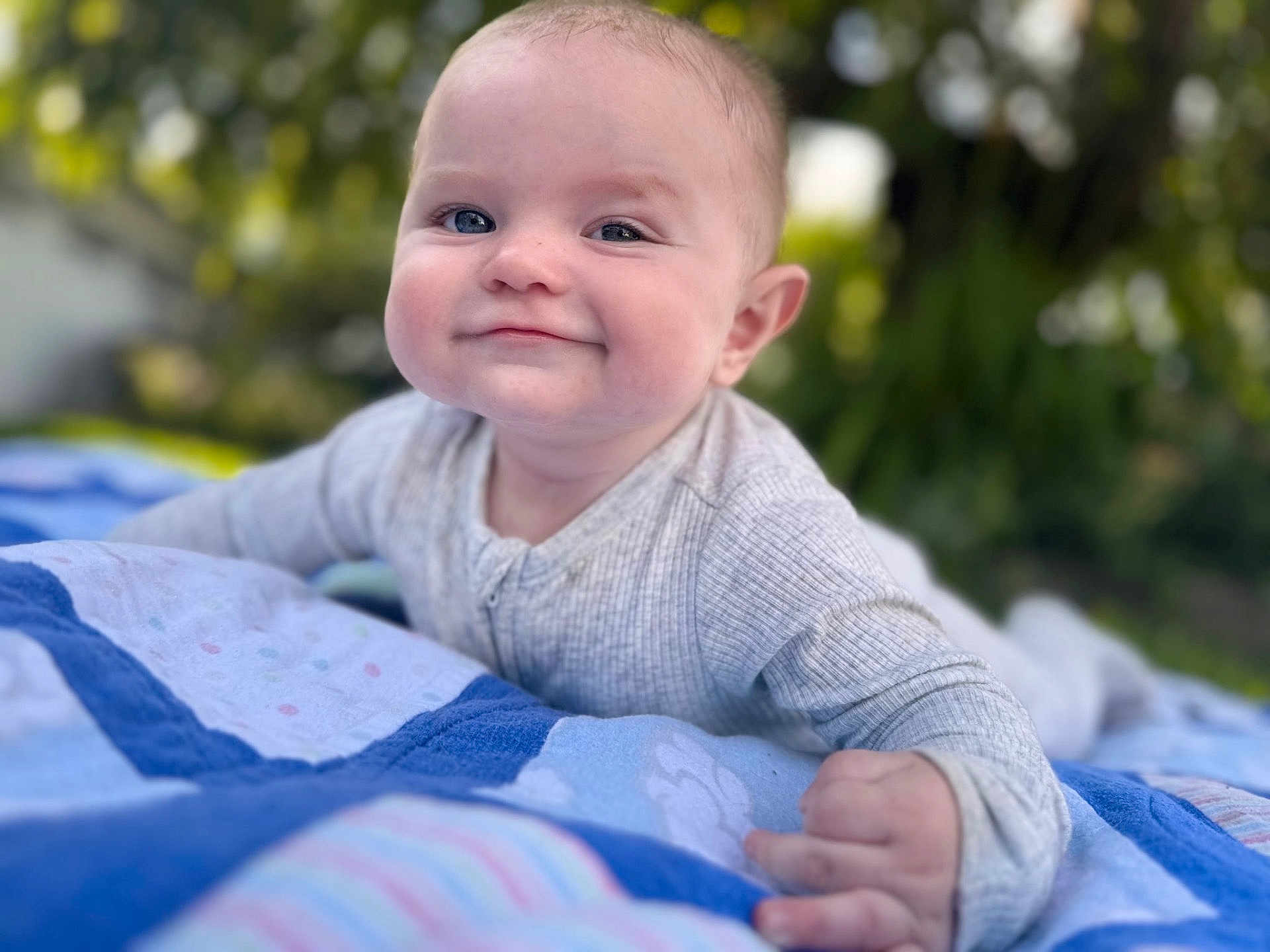 Braxton joined the competition — help win amazing prizes! baby, child, smile, face, outdoor, blanket, quilt, blue, gray_clothing, happy, toddler, cute, portrait, skin, hand, nature, greenery, daylight, infant, crawling