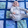 baby, child, infant, onesie, quilt, patchwork, smile, face, foot, playful, blue, green, pattern, fabric, blanket, cheeky, happy, lying_down, cute, indoors