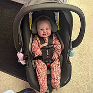 Hazel is registered to the contest to win money with this photo: baby, infant, car_seat, smiling, child, onesie, floral_pattern, indoor, flooring, carpet, tile, footwear, black_car_seat, safety_harness, happy, person, cute, seated, head_support, playful