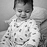 baby, bed, black_and_white, blanket, cozy, cute, eyelashes, face, hair, hand, infant, nursery, onesie, pajamas, pillow, playful, portrait, sitting, smile, toddler