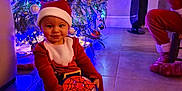 Noham a rejoint le concours — aidez-le/la à gagner de superbes lots ! baby, child, christmas_tree, christmas_lights, santa_hat, santa_outfit, toy, spiderman, ball, floor, tile_floor, festive_clothing, holiday, indoor, person, smile, decoration, red_clothing, blue_lights, happy