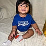 baby, bed, bedroom, blanket, blue_shirt, child, clothing, dark_hair, eyes, face, family, hands, happy, indoors, infant, legs, portrait, sitting, smiling, white_socks