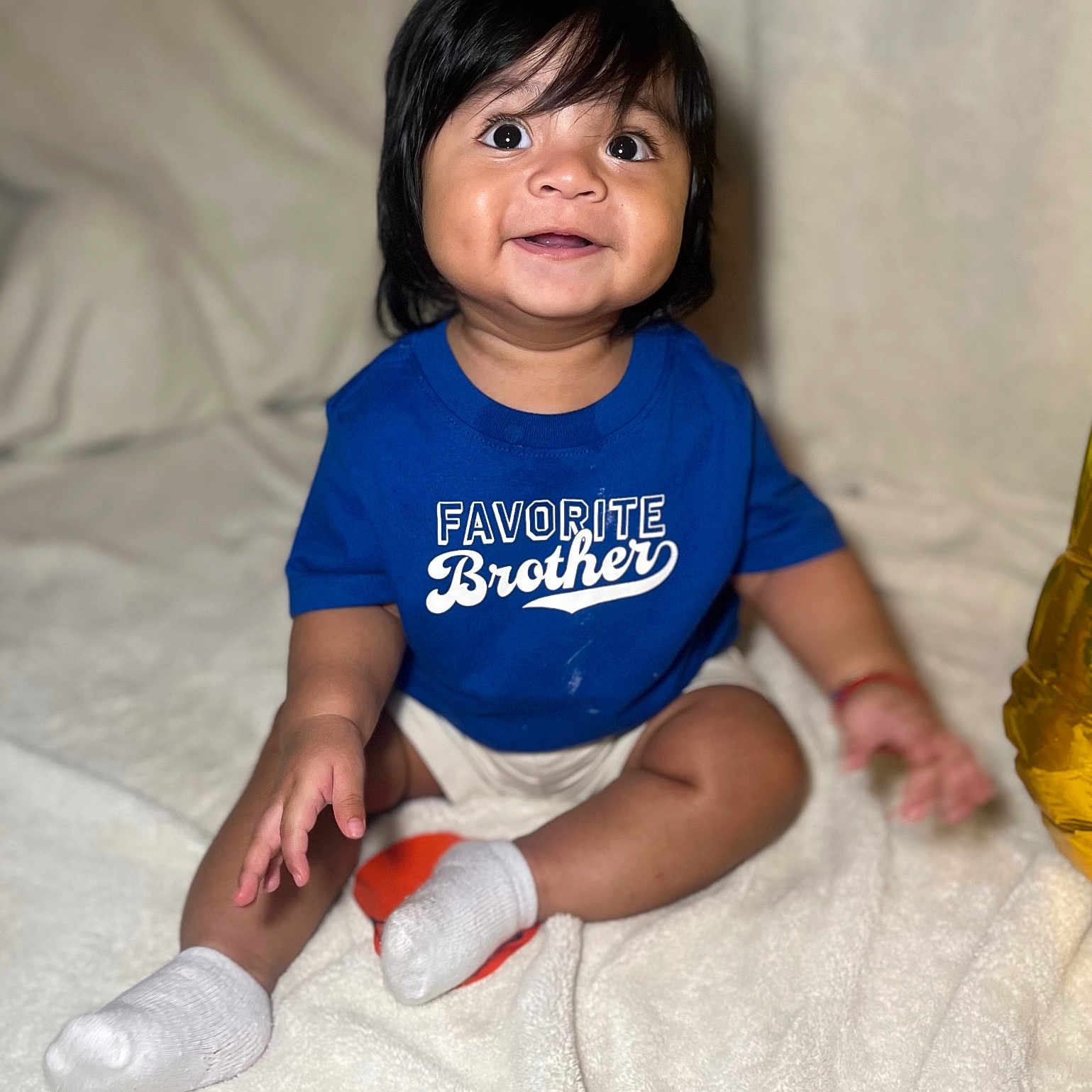 Ricardo Jr. joined the competition — help win amazing prizes! baby, bed, bedroom, blanket, blue_shirt, child, clothing, dark_hair, eyes, face, family, hands, happy, indoors, infant, legs, portrait, sitting, smiling, white_socks
