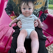 Truett joined the competition — help win amazing prizes! baby, child, adult, person, slide, playground, outdoor, tie_dye, cap, grass, woodchips, smile, blue_eyes, short_sleeves, holding, sitting, legs, feet, curly_hair, casual_clothing