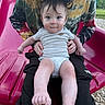 baby, child, adult, person, slide, playground, outdoor, tie_dye, cap, grass, woodchips, smile, blue_eyes, short_sleeves, holding, sitting, legs, feet, curly_hair, casual_clothing