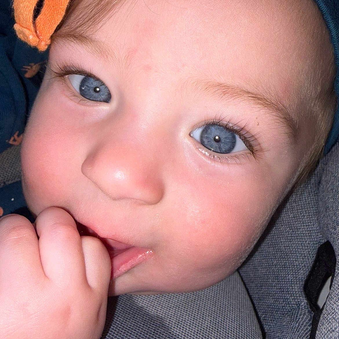 Truett is registered to the contest to win money with this photo: baby, close_up, blue_eyes, hand, fingers, hat, orange_bow, face, skin, child, infant, cute, portrait, sitting, seat, cozy, warm, expression, young, person