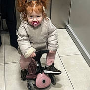 Ethel a rejoint le concours — aidez-le/la à gagner de superbes lots ! child, cute, hallway, indoor, jacket, pacifier, person, pigtails, pink_pants, play, red_hair, ride_on, small_vehicle, sneakers, standing, tile_floor, toddler, toy, warm_clothing, young_child