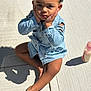 toddler, child, denim, blue_jacket, curly_hair, sidewalk, concrete, shadow, barefoot, baby_bottle, sunlight, outdoor, cute, sitting, hands_on_face, pensive, casual_clothing, young_child, portrait, daylight