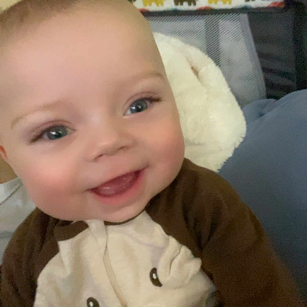Stiles is registered to the contest to win money with this photo: baby, blanket, clothing, coat, couch, crib, cushion, face, furniture, happy, head, homedecor, indoors, jacket, laughing, person, photography, portrait, sitting, smile