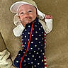 baby, infant, child, smiling, hat, star_pattern, blue_clothing, red_zipper, white_sleeves, hand_in_mouth, lying_down, beige_background, fabric_texture, cute, happy, portrait, one_person, indoors, casual_clothing, newborn