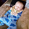 baby, sleeping, onesie, dinosaur_print, bib, couch, pillow, brown, child, infant, peaceful, indoor, soft_fabric, toddler, cute, relaxing, face, hand, person, cozy