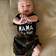 Hunter joined the competition — help win amazing prizes! baby, child, smiling, black_shirt, camo_shorts, socks, lying_down, beige_background, happy, infant, cute, face, hands, feet, clothing, portrait, indoors, playful, young_child, person