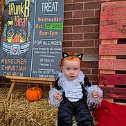 Aaliyah joined the competition — help win amazing prizes! toddler, child, costume, cat_ears, pumpkin, hay, sign, brick_wall, wooden_pallet, event, outdoor, fall, halloween, black_and_white, red_hair, person, portrait, cute, holiday, festival