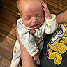 Samuel joined the competition — help win amazing prizes! baby, newborn, infant, sleeping, onesie, animal_print, hand, arm, person, wooden_floor, indoor, holding, casual_clothing, tshirt, comfort, peaceful, cute, child, portrait, human