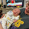baby, sleeping, pajamas, winnie_the_pooh, person, smiling, television, news, indoor, living_room, couch, sweatshirt, glasses, holding, child, cute, resting, face, human, home
