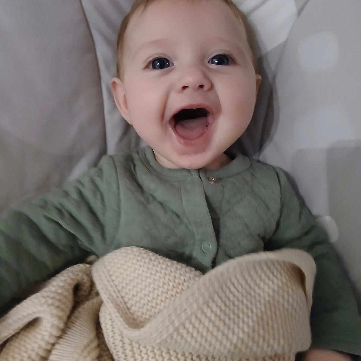Ellipsis is registered to the contest to win money with this photo: baby, bedding, blanket, blue_eyes, child, cute, fabric, face, hair, hand, happy, indoor, infant, knit_blanket, onesie, open_mouth, portrait, skin, sleeve, smiling