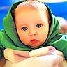 baby, blanket, blue_eyes, cheeks, child, closeup, colorful_background, cozy, expression, eyes, face, gaze, green_hoodie, hood, indoors, infant, portrait, skin, soft_texture, warm_lighting