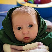 Ellipsis is registered to the contest to win money with this photo: baby, infant, child, face, blue_eyes, hoodie, blanket, portrait, closeup, cheeks, indoors, playroom, toys, ball, bokeh, soft_texture, cozy, gaze, watermark, cute_expression