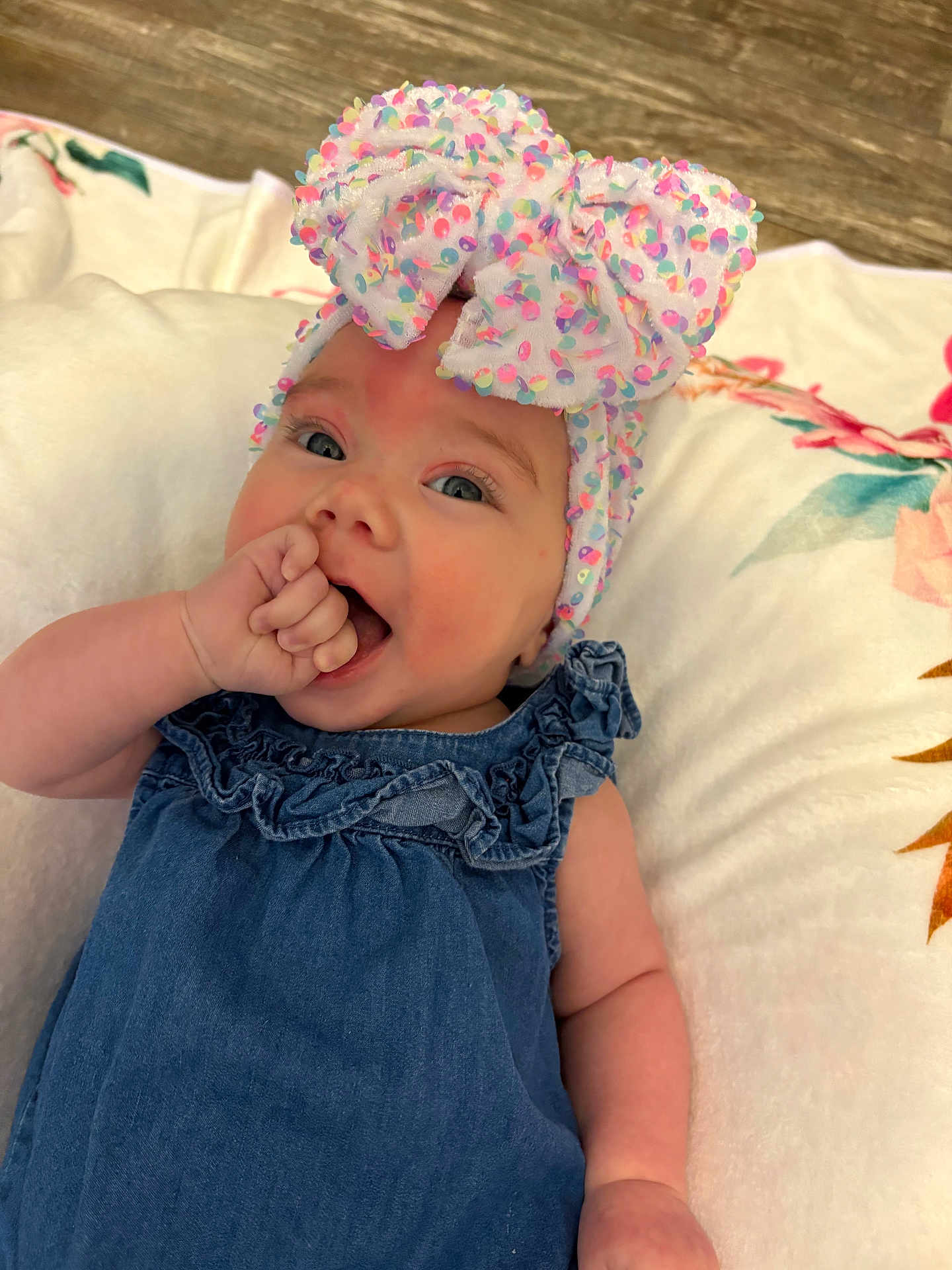 Hadley is registered to the contest to win money with this photo: baby, infant, child, headband, bow, blue_dress, thumb_sucking, cushion, floral_pattern, soft_texture, smiling, portrait, closeup, indoors, cute, happy, person, skin, headwear, relaxing