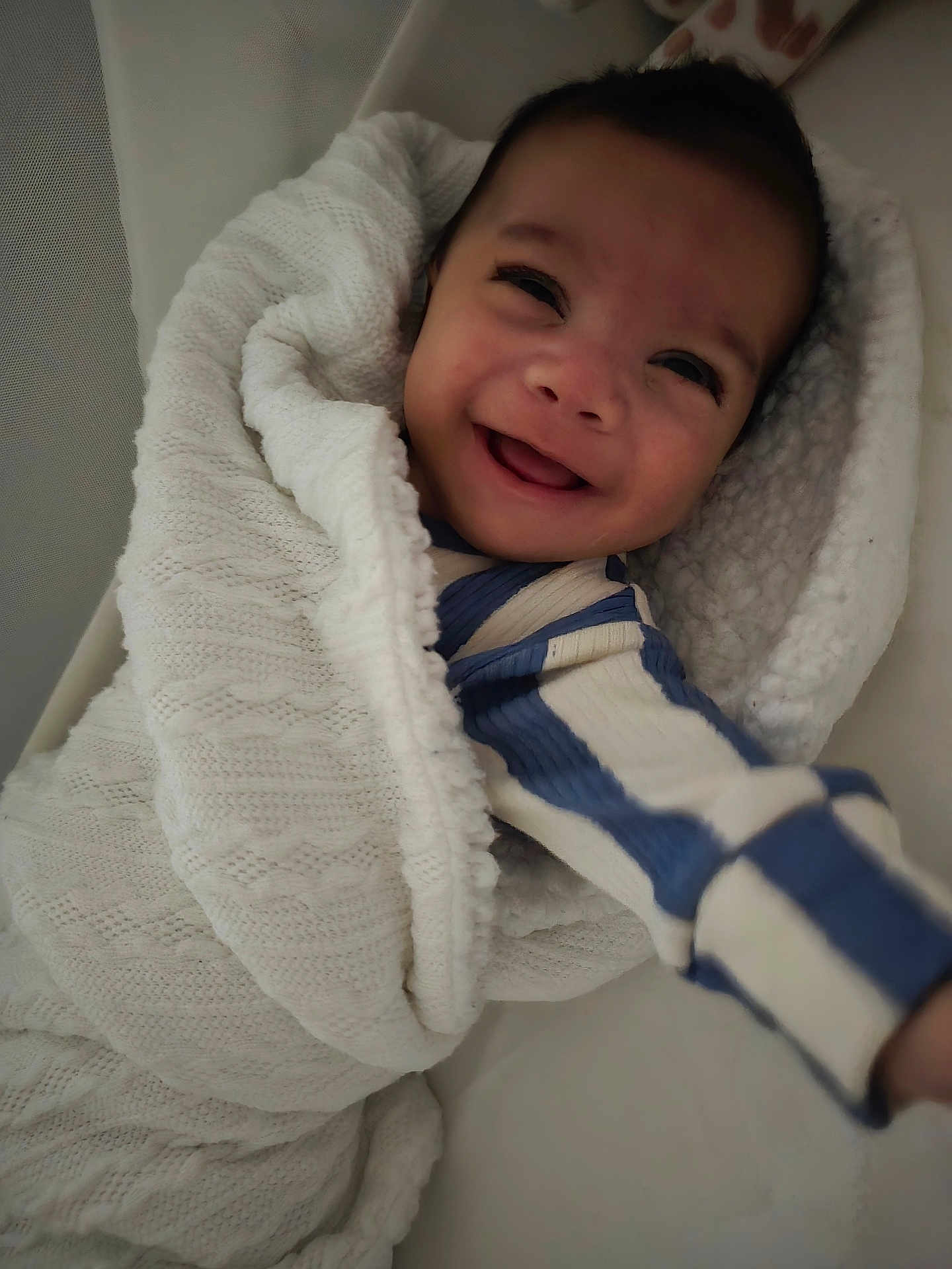 Dontae is registered to the contest to win money with this photo: baby, smiling, blanket, knitted, cozy, child, infant, reaching, striped_clothing, blue, white, happy, portrait, cute, warm, soft_lighting, closeup, wrapped, indoor, person