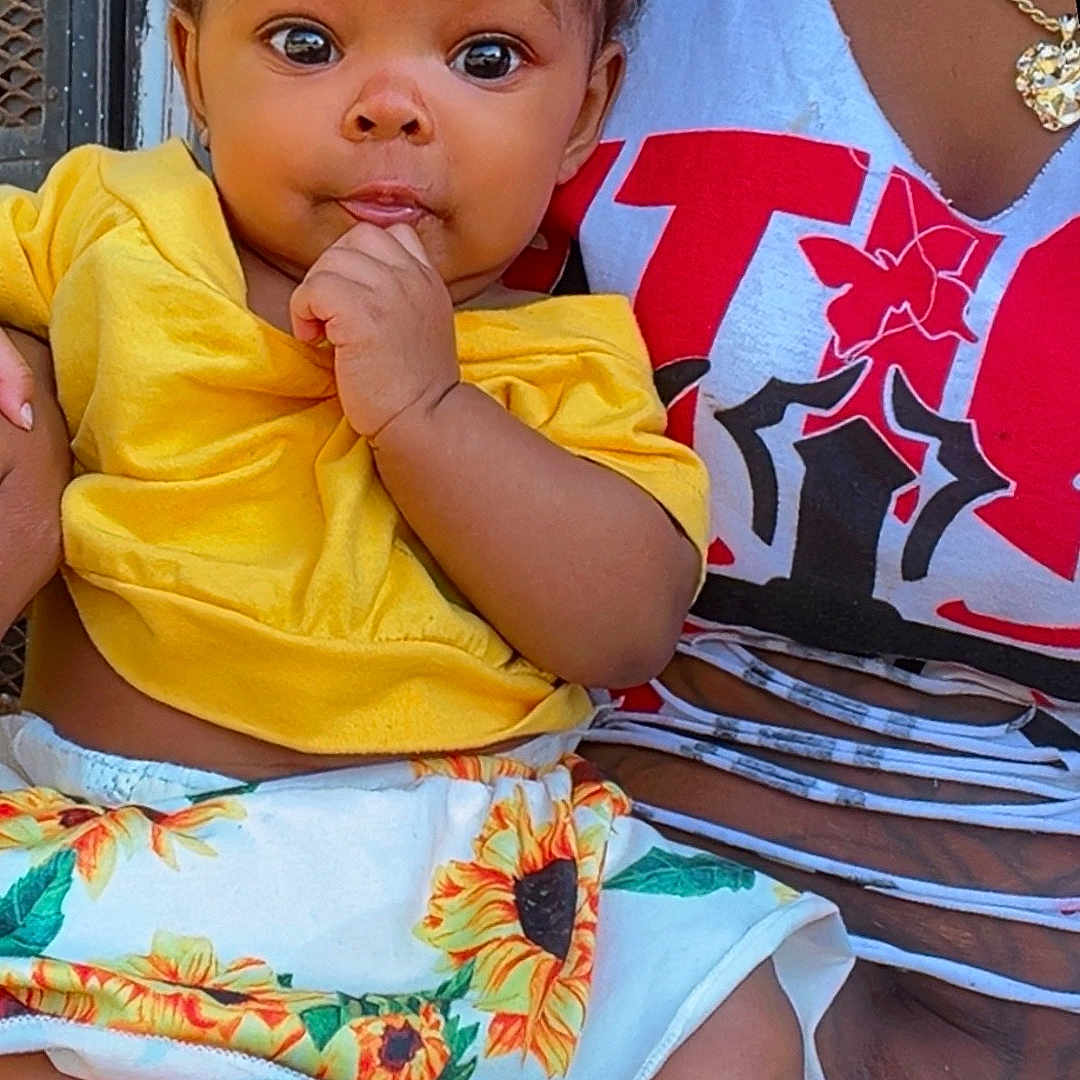 Kaliani joined the competition — help win amazing prizes! adult, baby, barefoot, child, curious, cute, eyes, face, fashion, hand, headband, holding, infant, necklace, outdoor, person, portrait, sitting, sunflower_skirt, yellow_clothing