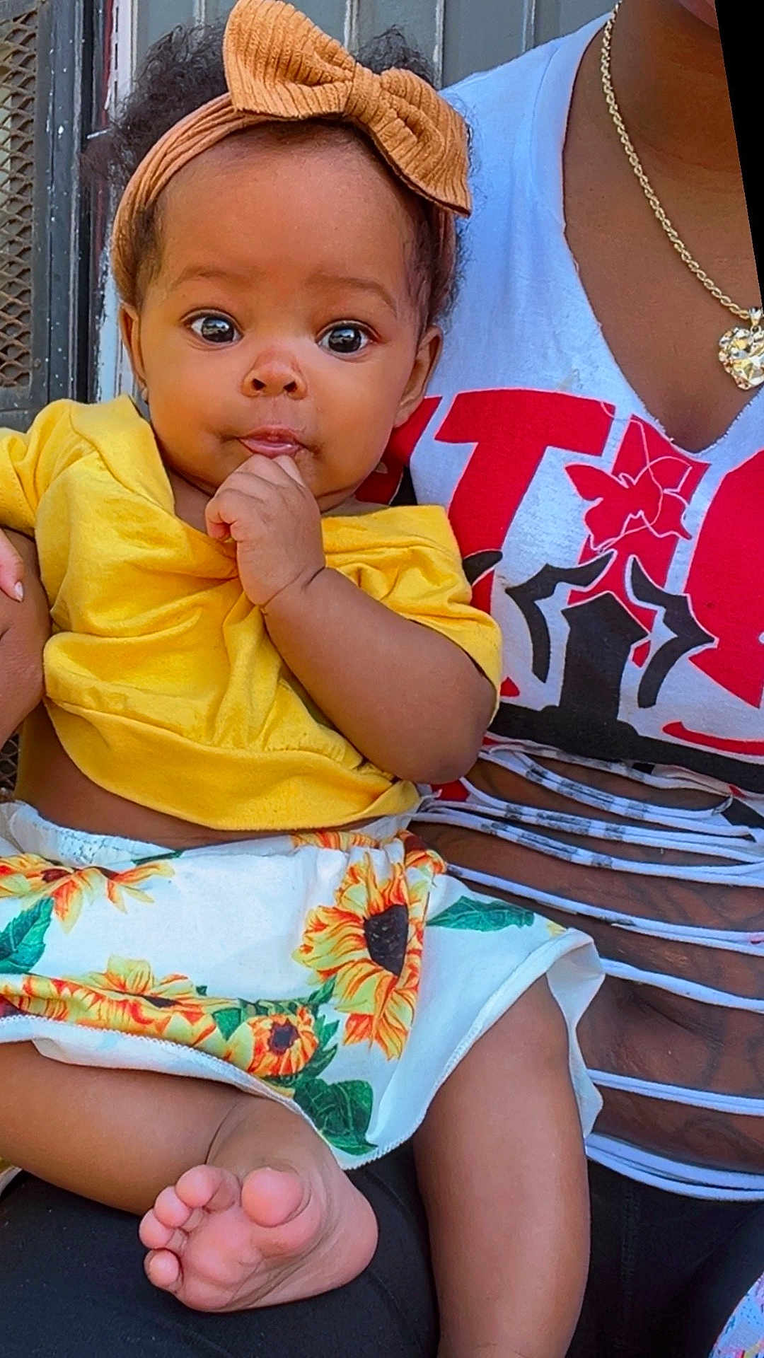 Kaliani joined the competition — help win amazing prizes! baby, child, infant, headband, yellow_clothing, sunflower_skirt, barefoot, hand, face, eyes, adult, necklace, sitting, curious, outdoor, person, fashion, cute, portrait, holding