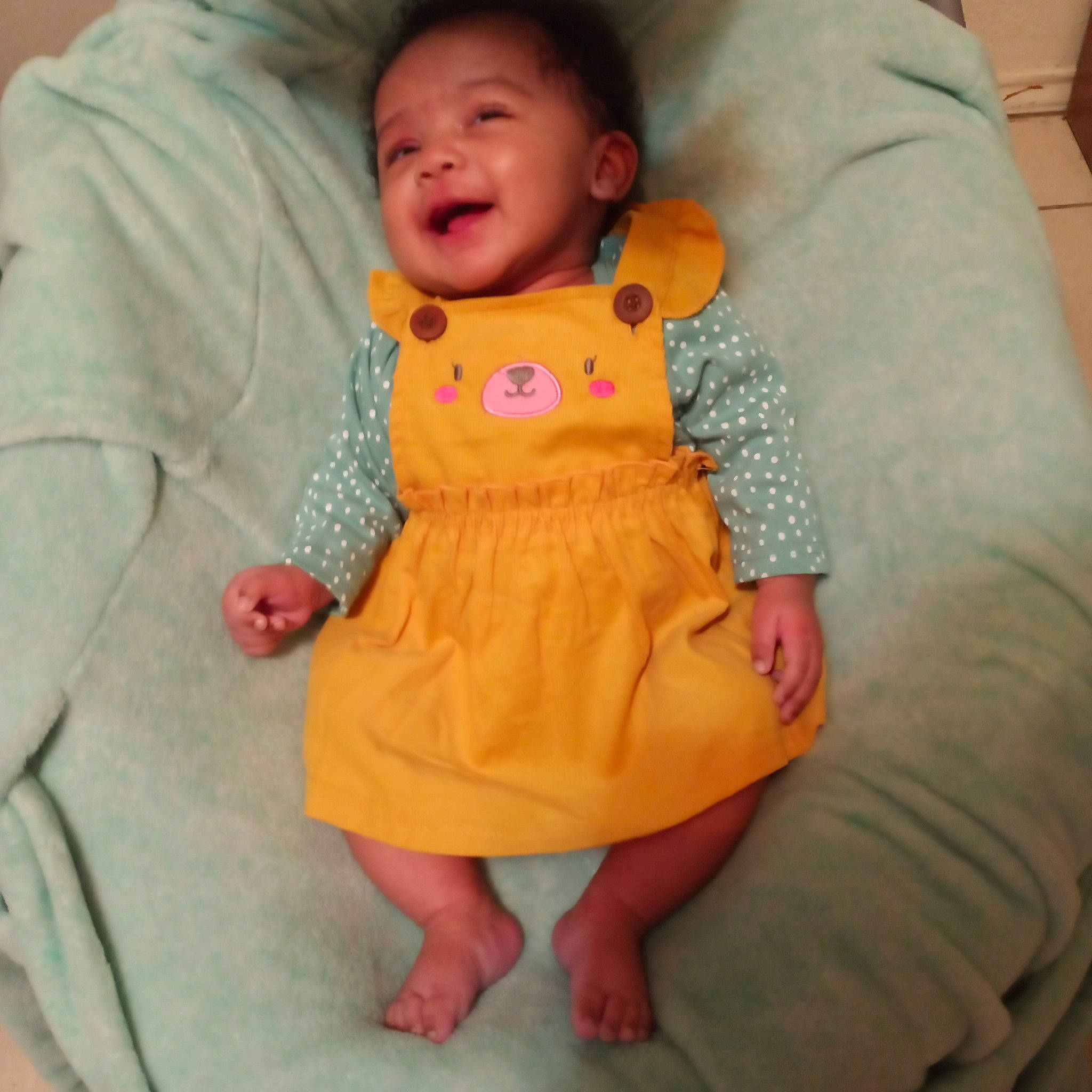 Amani is registered to the contest to win money with this photo: baby, baby_toddler_clothing, cheek, child, comfort, day_dress, face, happy, head, linens, one_piece_garment, outerwear, pattern, peach, person, pink, skin, sleeve, smile, textile