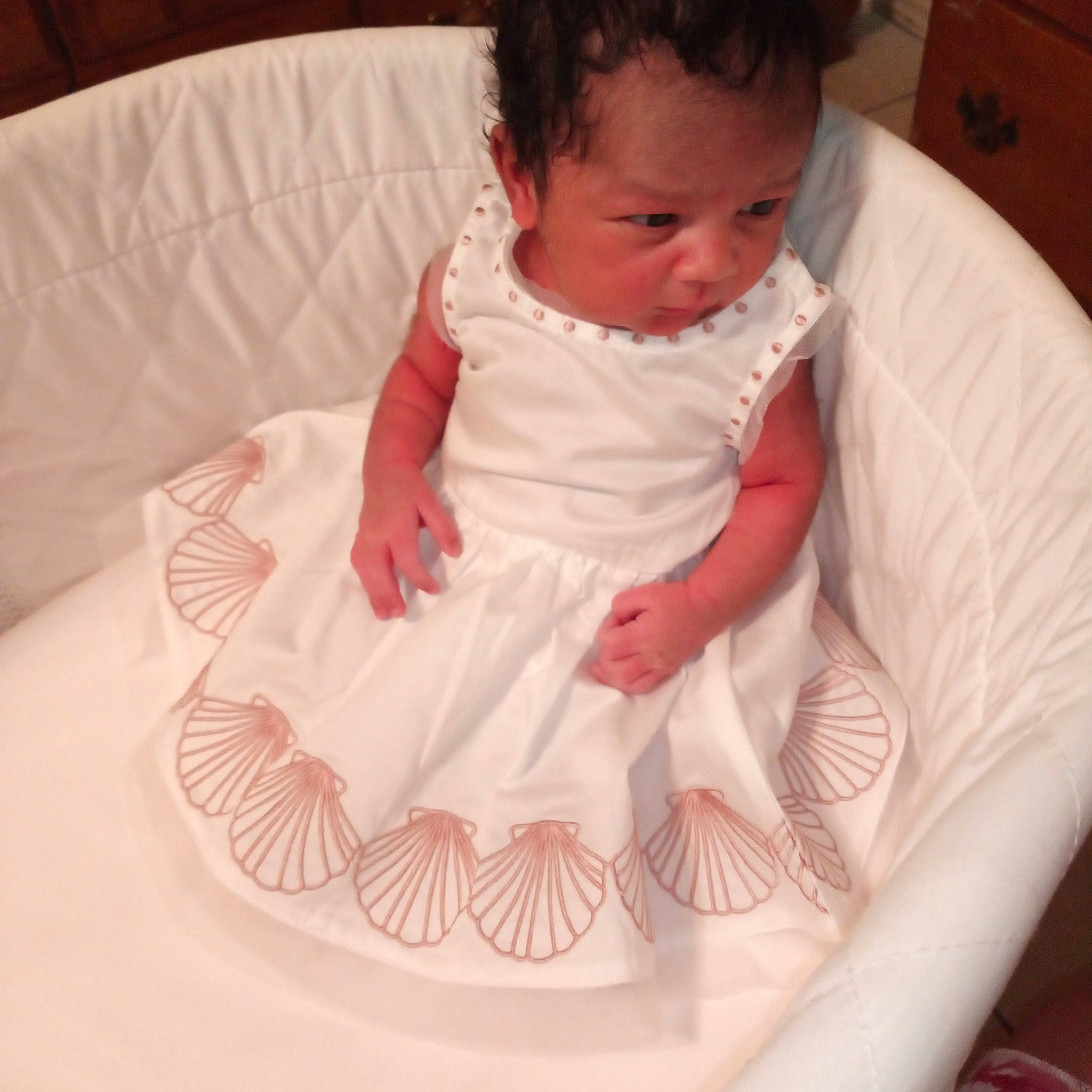 Amani is registered to the contest to win money with this photo: arm, baby, baby_products, baby_toddler_clothing, cheek, child, comfort, dress, face, hand, human_body, linens, neck, pattern, person, pink, sitting, sleeve, sugar_cake, textile