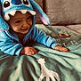 child, baby, toddler, smiling, blue_hoodie, character_hood, plush, couch, blanket, giraffe_print, toy_ring, numbers, hands, face, eyes, cozy, playing, indoor, soft_texture, portrait