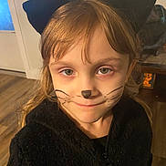 Lillian joined the competition — help win amazing prizes! black_ears, black_jacket, brown_hair, cat_costume, child, costume, cozy, cute, door, face_paint, floor, furniture, green_eyes, indoor, person, portrait, smile, warm_lighting, whiskers, young_child