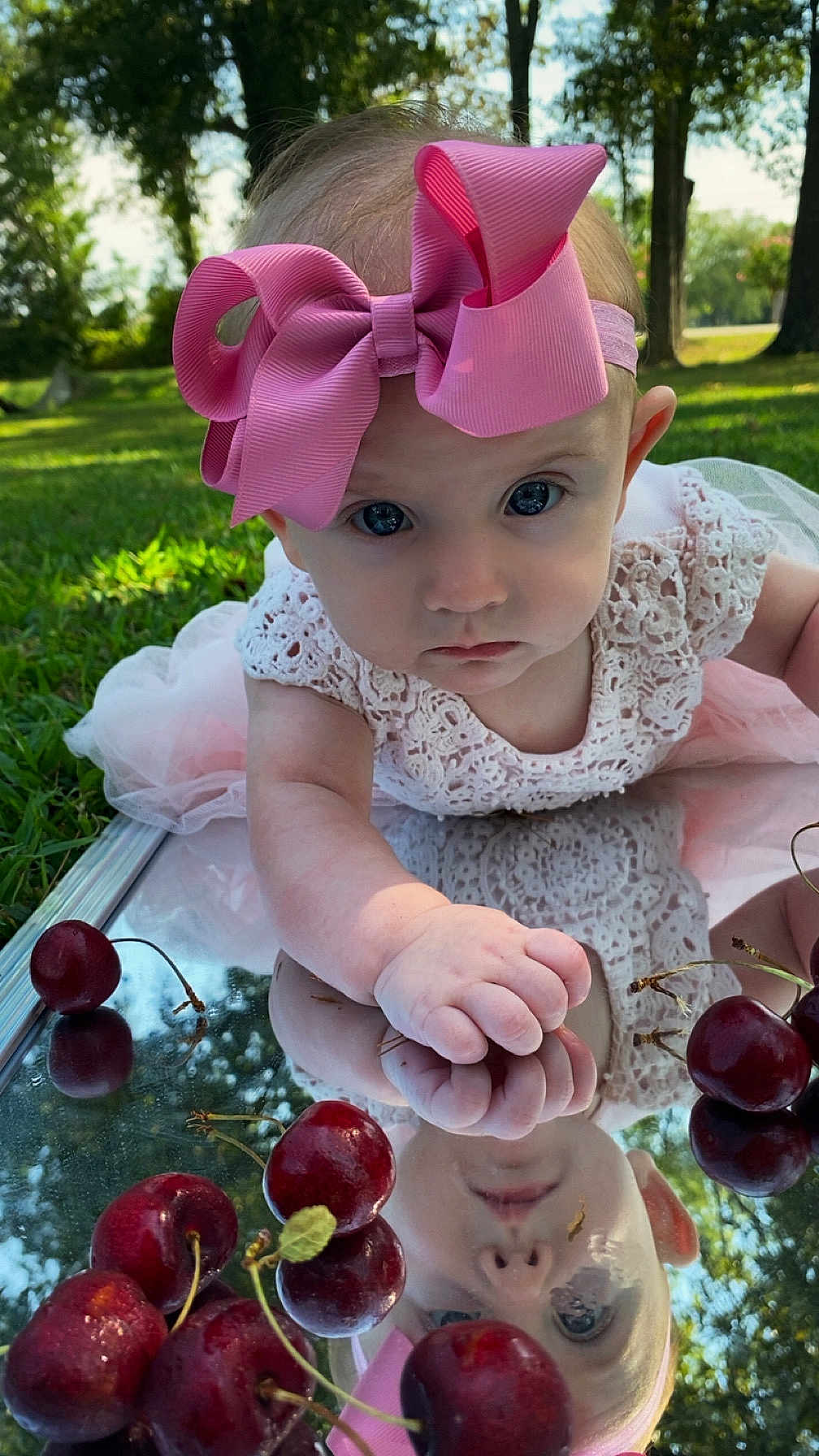 Nova is registered to the contest to win money with this photo: baby, pink_bow, reflection, cherries, outdoor, grass, toddler, cute, portrait, headband, curious, hand, nature, summer, dress, closeup, face, daylight, infant, mirror