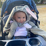 Nova is registered to the contest to win money with this photo: baby, child, stroller, bunny_costume, hood, ears, smile, outdoor, daylight, seat, face, blue_eyes, cute, clothing, grace_brand, person, playful, park, autumn, fun