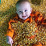 Nova is registered to the contest to win money with this photo: baby, child, corn, orange_clothing, pumpkin_pattern, smile, happy, cute, infant, fall, autumn, yellow, texture, face, hand, lying_down, playful, festive, portrait, clothing