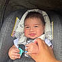 baby, car_seat, infant, smile, hand, pacifier, child, safety_harness, clothing, person, cute, portrait, indoor, holding_hand, seat_belt, head_support, happy, toddler, skin, face