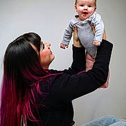 Amélia a rejoint le concours — aidez-le/la à gagner de superbes lots ! baby, child, woman, holding, smiling, indoor, casual_clothing, long_hair, pink_hair, black_hair, jeans, onesie, happy, face, person, portrait, joy, love, family, interaction