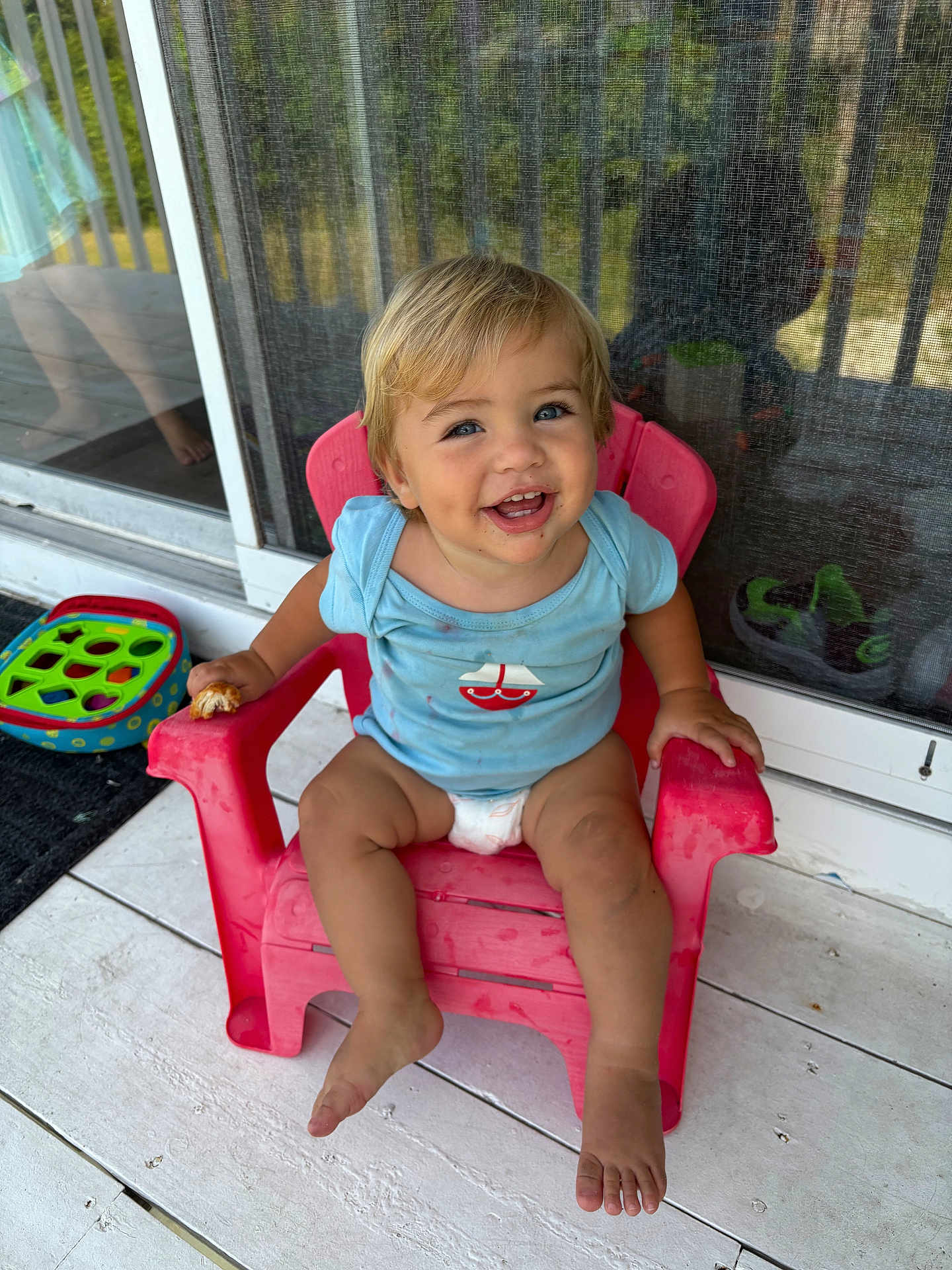 Thomas is registered to the contest to win money with this photo: toddler, child, smiling, blue_eyes, blond_hair, plastic_chair, blue_shirt, sailboat_design, snack, porch, sliding_door, screen_door, toy, barefoot, happy, sitting, outdoor, daylight, cute, young_child