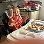 Thomas is registered to the contest to win money with this photo: toddler, child, high_chair, glass, food, pasta, plate, fork, bread, messy, kitchen, clutter, cabinet, table, red_shirt, smile, happy, indoor, person, meal