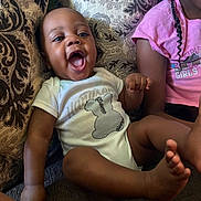 Makari joined the competition — help win amazing prizes! baby, infant, child, toddler, smiling, laughing, portrait, sitting, couch, sofa, cushion, indoors, home, pink_shirt, braids, onesie, barefoot, family, happy, closeup