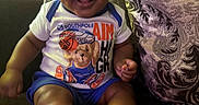 Makari is registered to the contest to win money with this photo: baby, child, smiling, sitting, portrait, indoor, couch, cushion, blue_hat, tshirt, shorts, teddy_bear, basketball, barefoot, feet, happy, infant, living_room, patterned_fabric, photography