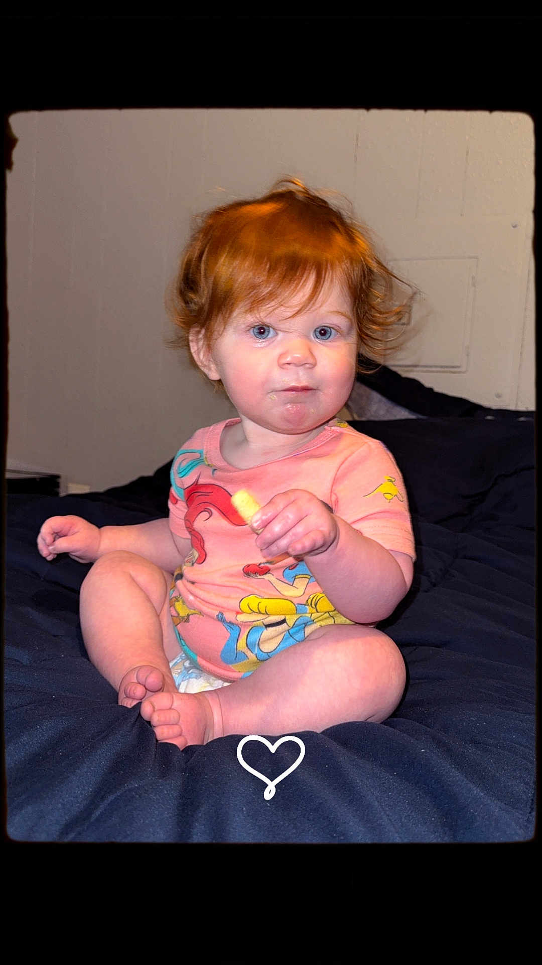 Georgia is registered to the contest to win money with this photo: toddler, child, red_hair, snack, sitting, curious_expression, colorful_clothing, indoor, blanket, cross_legged, cute, face, blue_eyes, hair, person, young_child, comfort, home, portrait, baby