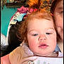 Georgia is registered to the contest to win money with this photo: adult_partial, baby, background, child, close_up, clothes, clothing, curious, cute, decor, face, glitter, home, indoor, light_skin, person, pony_tail, portrait, red_hair, sofa